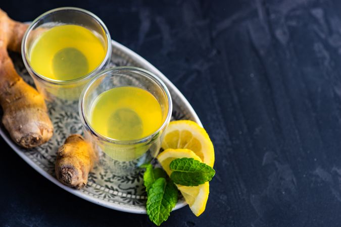 Two yellow detox drinks on silver tray with ginger and lemon