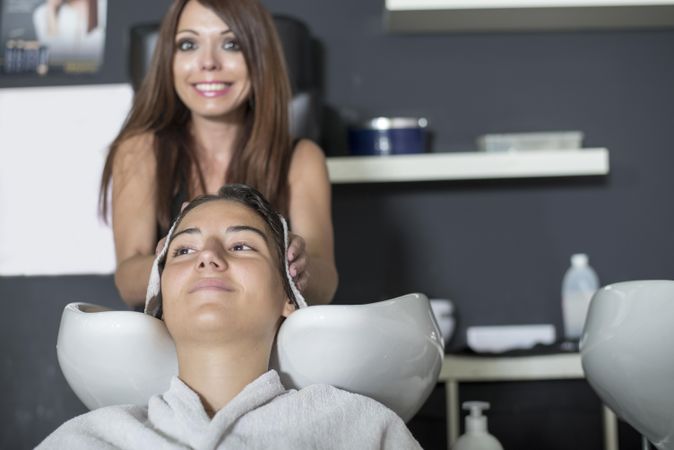 Hair stylist drying hair of woman with head in sink
