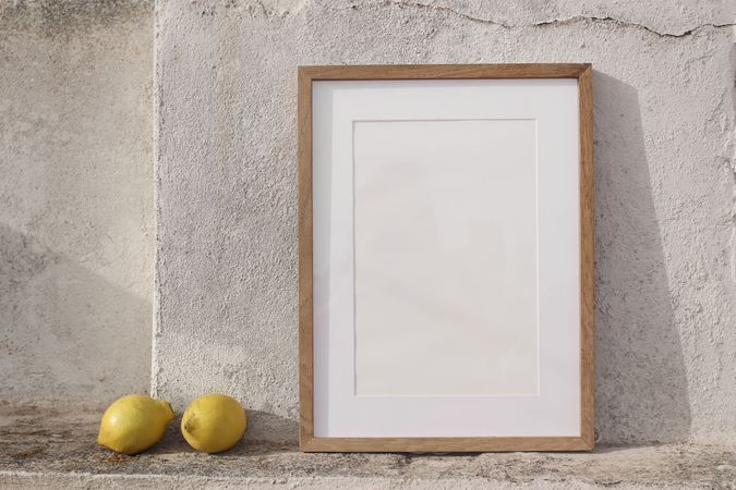 Minimal empty vertical wooden frame picture mockup against old textured wall in sunlight with fresh yellow lemons