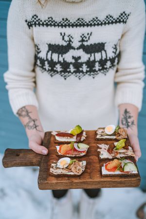 Cropped image of woman in Christmas sweater holding a wooden plate of tapas