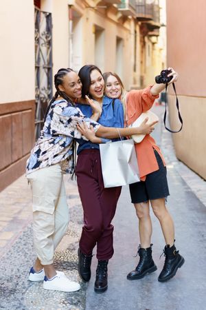 Three happy women in lane taking selfie with camera, vertical