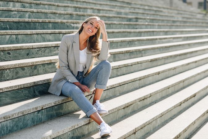 Woman in blazer sitting on outdoor steps on sunny day