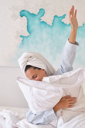 Positive woman embracing pillows on bed in morning