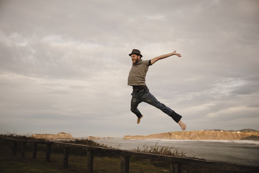 Young man in hats having fun on seat on coast near waving sea and cloudy sky