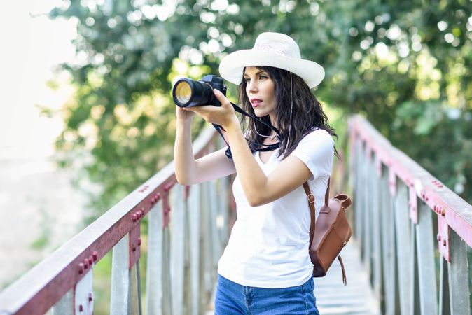 Woman taking photographs with a mirrorless camera, wearing straw hat outside