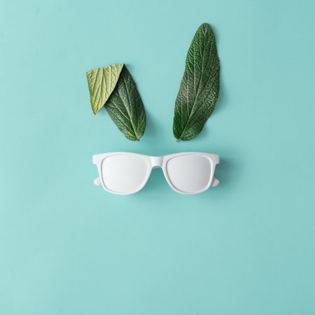 Bunny rabbit face made of natural green leaves with sunglasses on pastel blue background