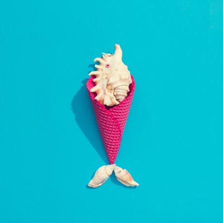 Sea shell in pink waffle cone on bright blue background