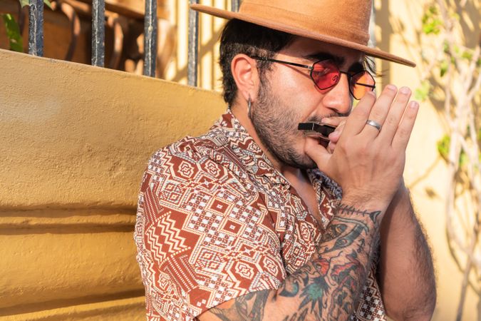 Latino musician playing harmonica standing on the street