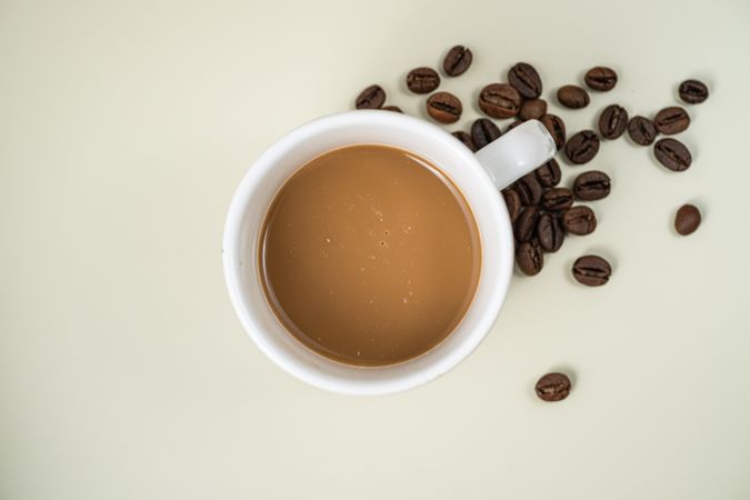 Flat lay of a cup of coffee with coffee beans on a light background