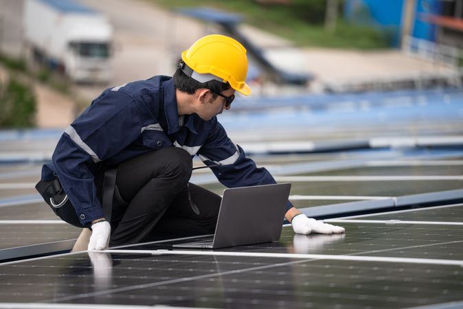 Engineer checking solar cell  or photovoltaic cell by computer laptop installed on the roof of the factory. Technician worker repair or inspect the system. Industrial renewable energy concept