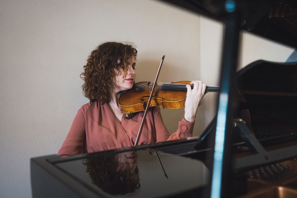 Pregnant woman playing on violin near piano in room