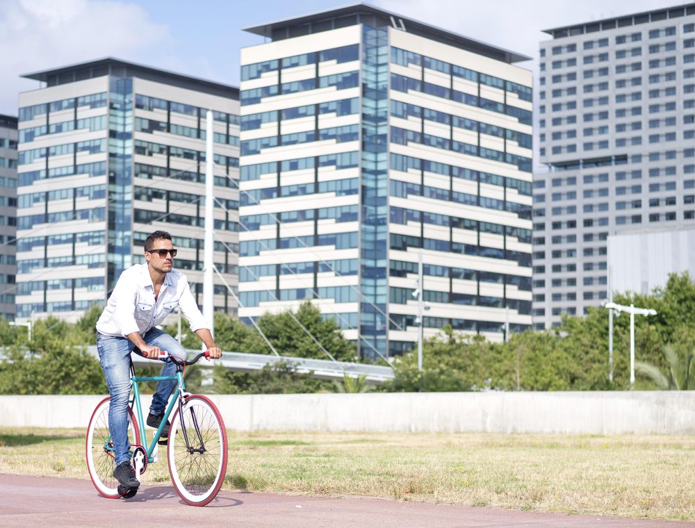 Male riding red and green bike outside next to buildings