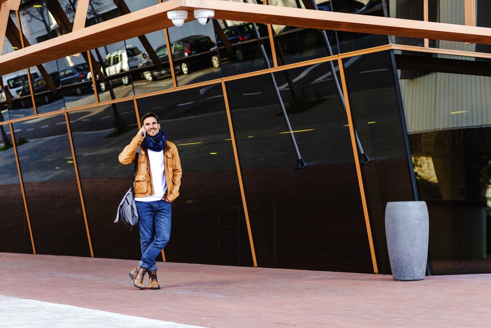 Stylish guy using smartphone outside modern building