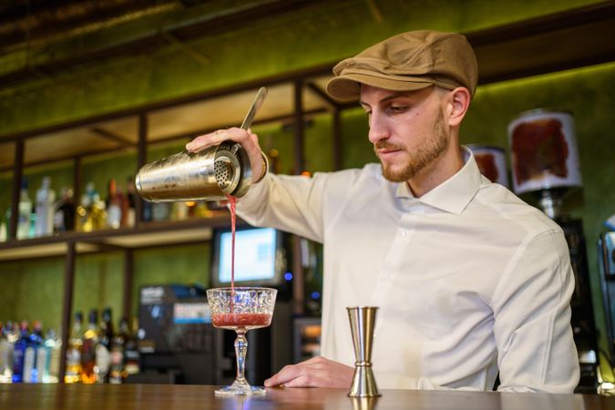 Man pouring red cocktail into glassware from shaker