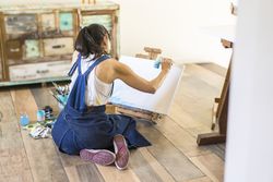 Woman artist painting on a canvas a blue abstract painting. Creative ywoman working on the floor in her art studio.