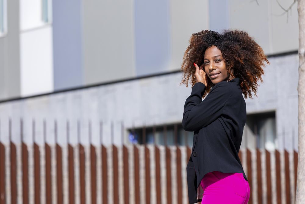 Black female putting her hair behind her ear while standing outside in the sun