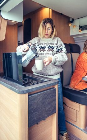 Women in warm sweater pouring coffee from moka in back of van, vertical
