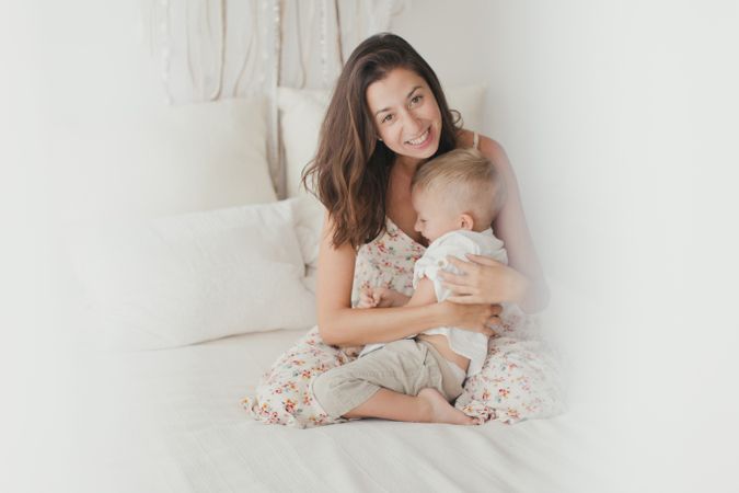 Mother ticking little son and laughing on bed