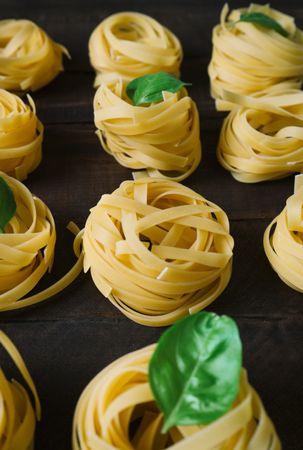Rows of raw tagliatelle pasta with basil leaves on table