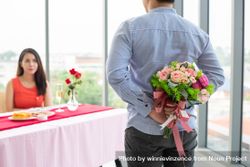 Man hiding bouquet from woman behind his back during romantic meal bE3mA5