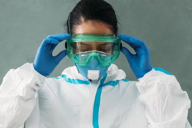 Female doctor in PPE gear and medical hazmat suit adjusting her eye wear