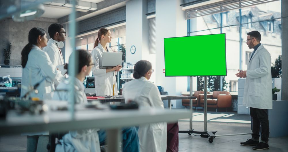 Group of Students Listening to Their Robotics Professor Who Uses Green Screen Monitor in a Laboratory.