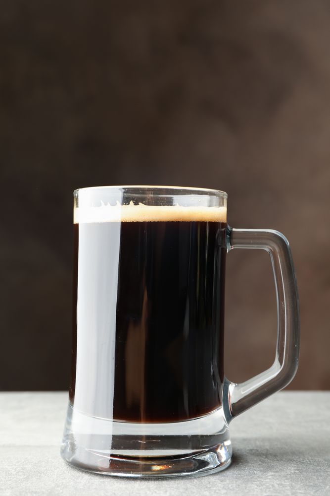 Glass of dark beer on grey table, space for text