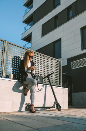 Businesswoman using mobile with her scooter next