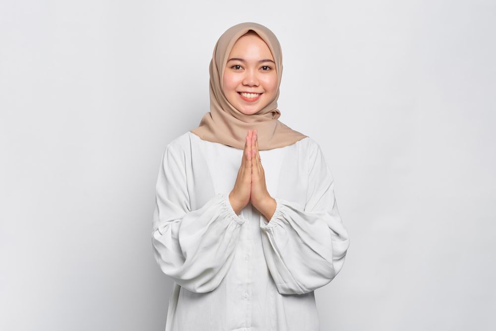 Happy Muslim woman in headscarf and light blouse with hands together in prayer
