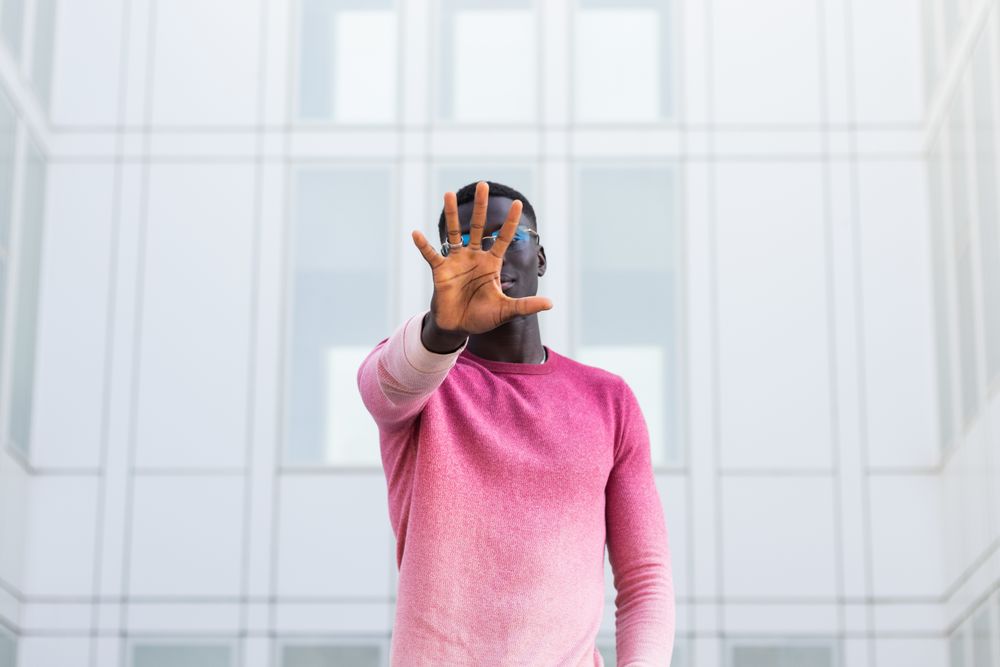 Black man covering face and showing stop gesture in city street