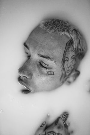 Moody portrait of young man with face tattoos submerged in milky water