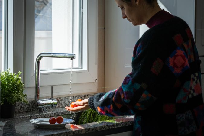 Woman washing tomato over sink