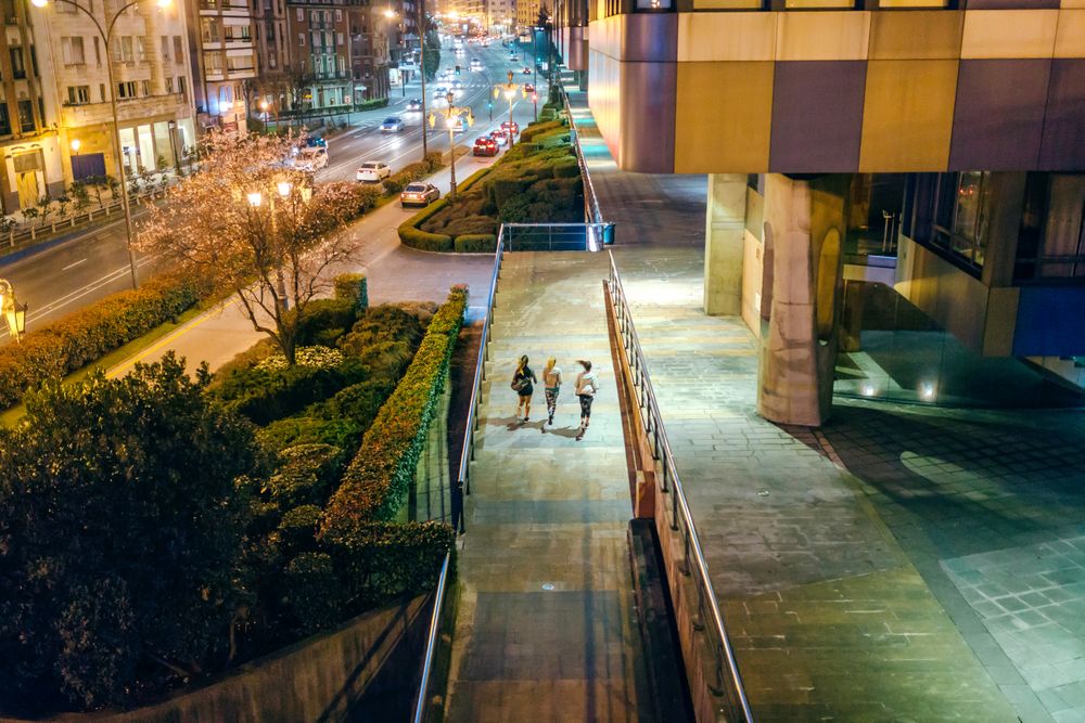 Looking down at back of female runners training together over city runway at night