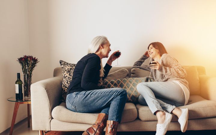 Mother and daughter relaxing on a couch talking while drinking wine