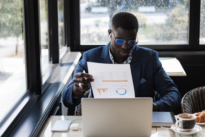Serious Black businessman in earbud with diagram on paper indoors
