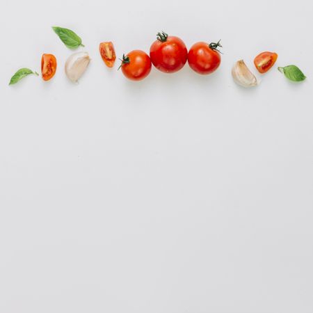 Whole and sliced cherry tomatoes, garlic clove, basil on light background