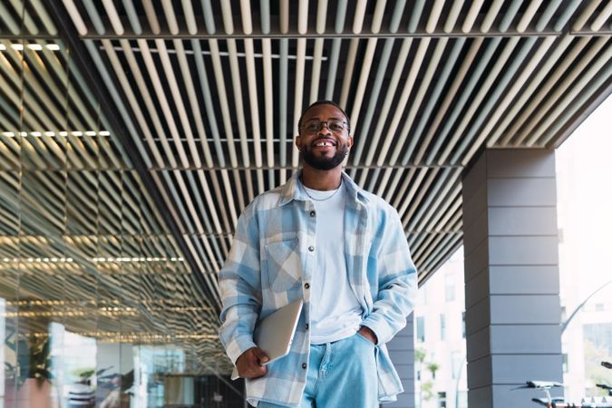 Joyful Black man with laptop near building