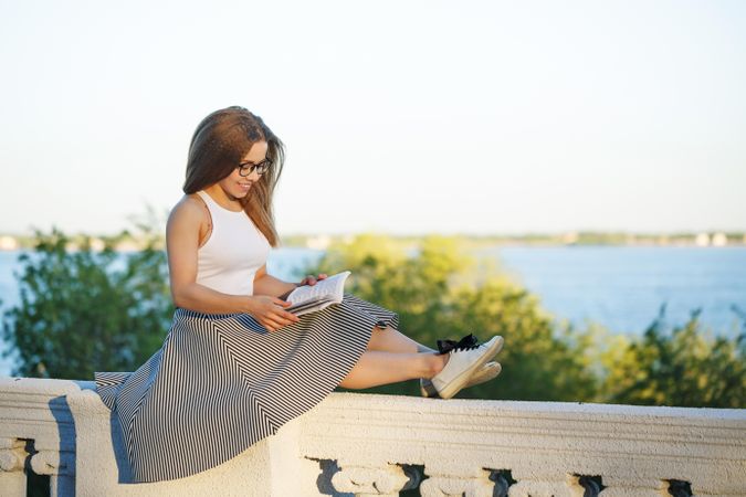 Woman perched atop a wall reading a book