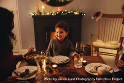 Boy sitting in front of fireplace having Christmas dinner with family 5XWkQ0