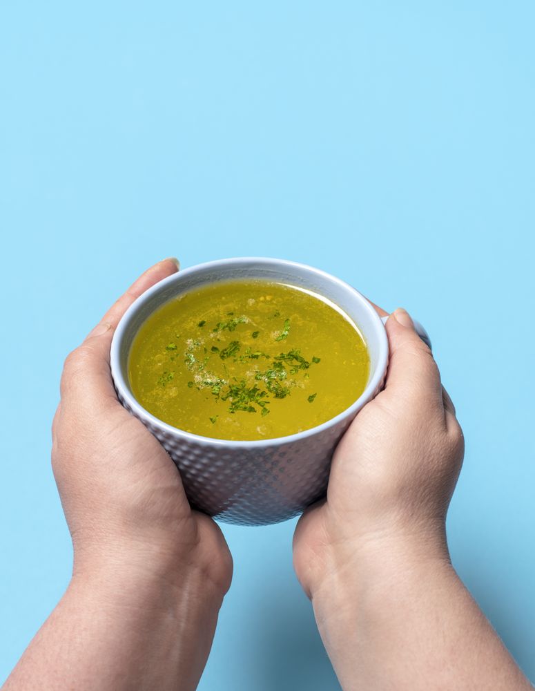 Chicken soup mug in woman hands on a blue background