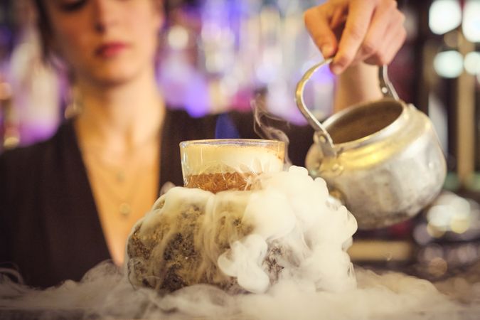 Crop female bartender preparing creative flaming cocktail in nig