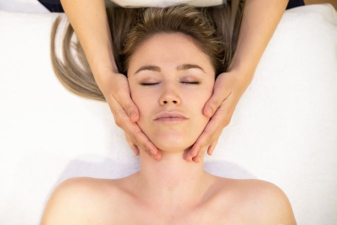 Young woman with masseuse working on her cheeks in a spa