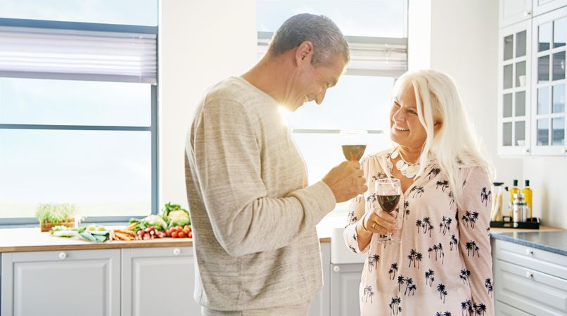 Couple toasting red wine in a bright kitchen with vegetables on the counter