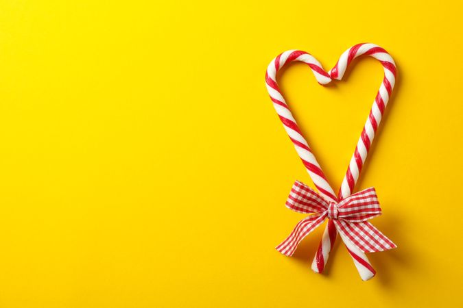 Sweet candy canes with bow on yellow background, space for text
