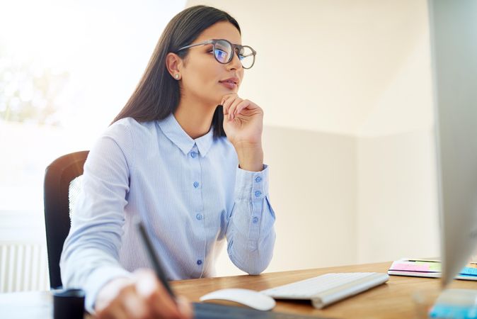 Woman in blue shirt and glasses working at her desk