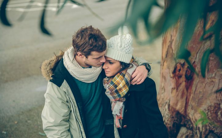 Cute couple in winter coats embracing under tree