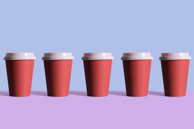 Single row of disposable coffee cups on blue and purple background