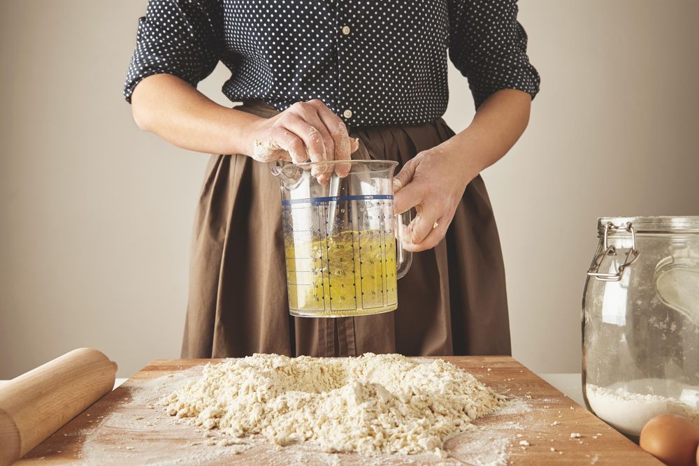 Woman stirring oil and water in measuring cup over pile of dough