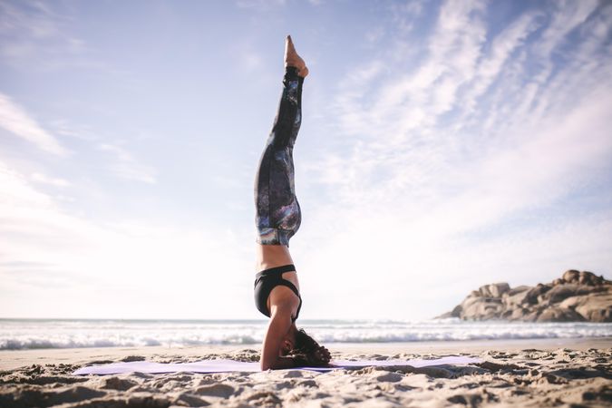 Side view of woman doing headstand on the beach