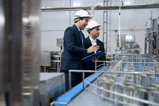 A businessman inspecting canned fish on conveyor belt at the factory